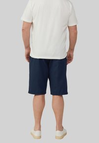 T-shirt blanc à manches courtes, shorts bleu marine et baskets légères. Le T-shirt a une texture lisse ; les shorts sont amples avec des poches latérales.