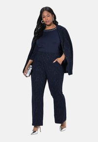 Marindress med ett strukturerat mönster, som har en kortärmad topp och skräddarsydda byxor. Silverdetaljer på skor och väska.