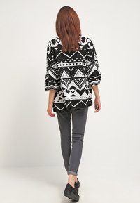 Übergroße schwarze und weiße jacke mit geometrischen Mustern, kombiniert mit grauen Slim-Fit-Jeans und schwarzen Plateauschuhen.