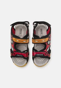 Sandali rossi e neri con accenti gialli, cinturini in Velcro e una soletta decorata. Presentano un materiale traspirante e una suola robusta.