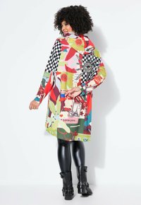 Kleurvolle oversized jurk met verschillende patronen, waaronder bloemmotieven, geruite elementen en tekst. Zwarte leggings en enkelboots maken de look compleet.