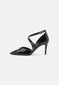 Escarpins à talons hauts en cuir verni noir, avec un bout pointu, dotés de lanières croisées et de boucles dorées. Hauteur de talon de 3 pouces.