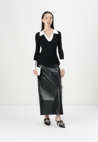 Zwart longsleeve shirt met een witte kraag, gecombineerd met een zwarte leren maxi rok. Accessoires zijn een witte clutch en zwarte hoge hakken.
