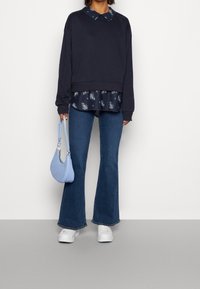 Námořnický svetr s límečkem vrstvený přes dlouhou košili s květinovým vzorem, doplněný o rozšířené modré džíny, bílé tenisky a svetřík světle modré barvy.