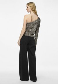 Top con una spalla in paillettes metalliche che presenta una superficie testurizzata e scintillante; abbinato a pantaloni neri larghi e svasati.