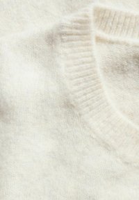 Ljusbeige tröja med rund hals och ribbad mudd. Tyget verkar mjukt och har en fint strukturerad stickning.