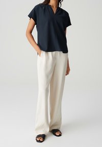 Blouse à manches courtes bleu marine foncé avec un décolleté en V. Associée à un pantalon large couleur crème clair. Le modèle porte des sandales plates noires.