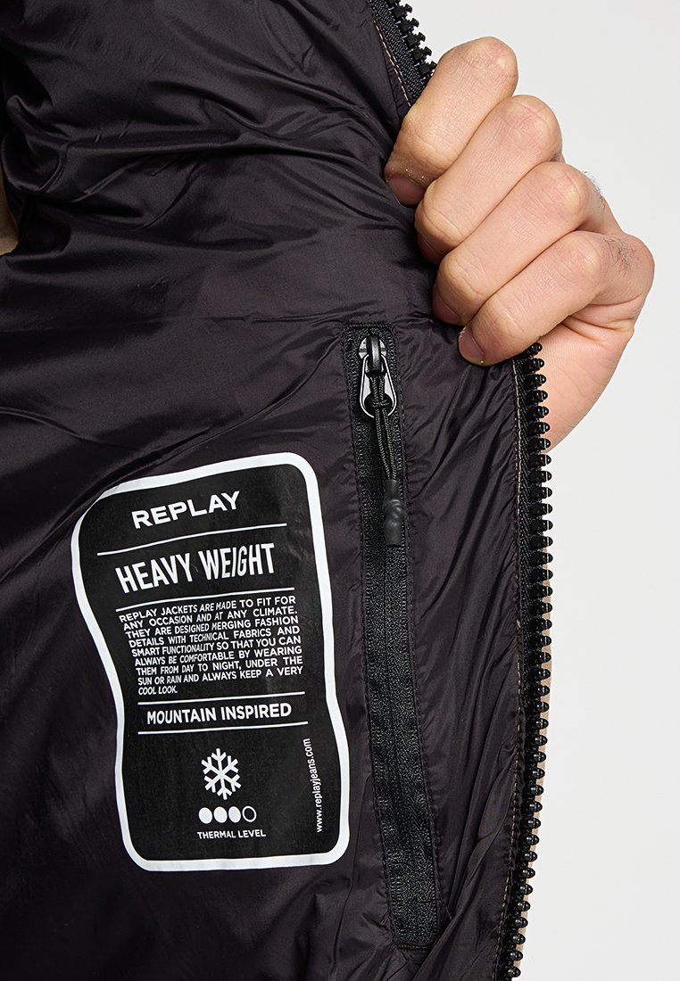 Schwarze isolierte Jacke mit einem Reißverschlusstascheninneren. Das Etikett trägt die Aufschrift "REPLAY HEAVY WEIGHT" und beschreibt die Funktionen und das thermische Niveau.