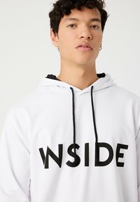 Sudadera blanca con cordones negros y un gran gráfico negro "WSIDE". Tela suave, mangas largas y un corte relajado.