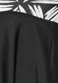 Svart tyg med en slät textur och draperad design, med ett kontrasterande vitt lövmönster upptill. Höga sömmar och enkla linjer.