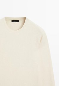 Maglione beige chiaro con motivo a maglia testurizzata, scollo rotondo e polsini a coste. Il materiale sembra morbido e traspirante. Etichetta del marchio visibile.