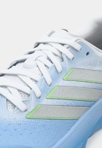 Αθλητικό παπούτσι ανοιχτού μπλε χρώματος με λευκά κορδόνια. Διαθέτει τρεις ασημένιες ρίγες και πρασινωπή λεπτομέρεια. Κείμενο στο επάνω μέρος με υφή και μαλακή σόλα.