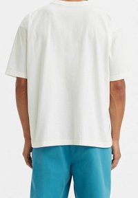Camiseta de algodón blanca con un corte relajado, mangas cortas y escote redondo, con un diseño en la parte posterior liso, sin patrones ni adornos.