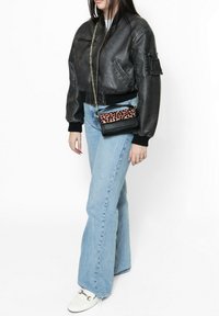 Giubbotto bomber in pelle nera con polsini a coste, jeans svasati blu chiaro e una piccola borsa nera con un accento in stampa leopardata rosa.