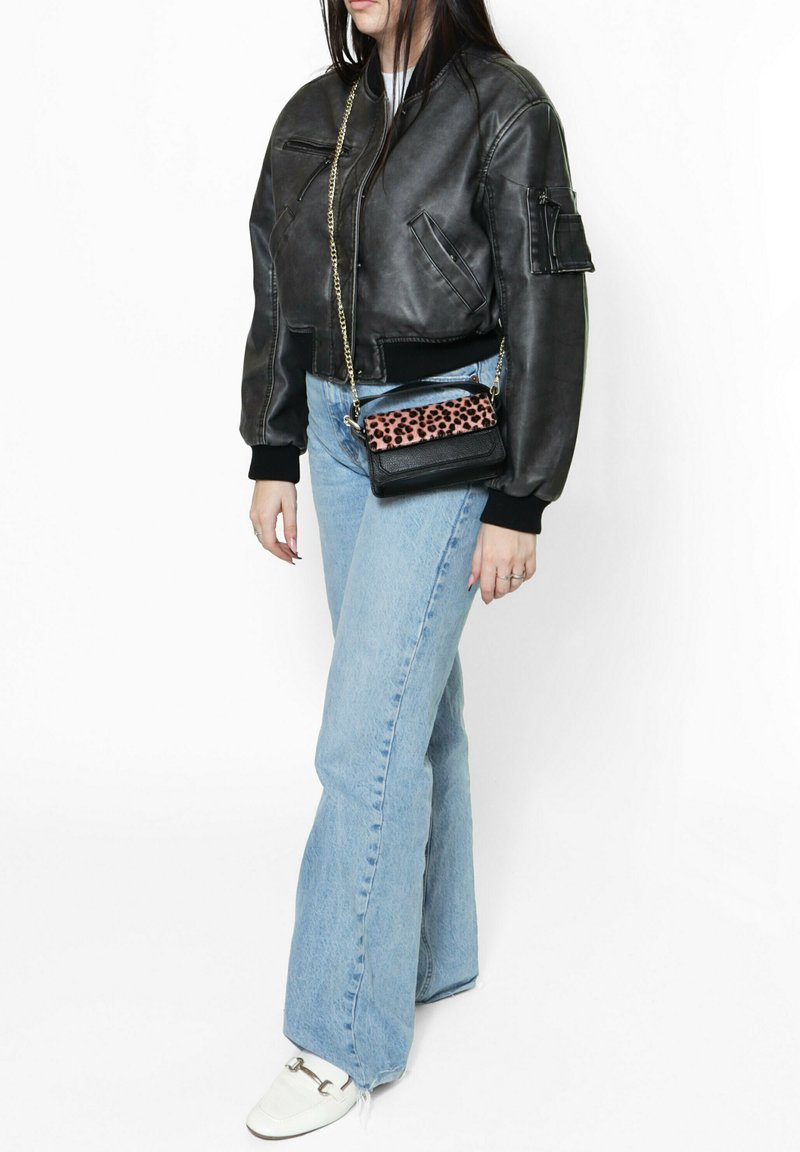 Giubbotto bomber in pelle nera con polsini a coste, jeans svasati blu chiaro e una piccola borsa nera con un accento in stampa leopardata rosa.
