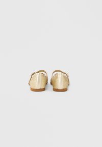 Παπούτσια με χρυσό γκλίτερ και λείο μεταλλικό λουράκι, πίσω όψη, με χαμηλό τακούνι και στρογγυλεμένη μύτη.