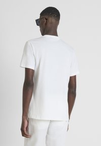 Camiseta blanca de algodón con mangas cortas y escote redondo, combinada con pantalones ligeros de color crema. Diseño minimalista sin patrones.