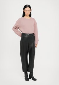 Lichtroze oversized trui met een ronde hals, gecombineerd met high-waisted zwarte nepleer broek en zwarte haklaarzen.