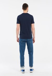 Námornícky modré tričko s krátkymi rukávmi, skombinované so svetlomodrými džínsami. Tričko má okrúhly výstrih; džíny majú klasický rovný strih.