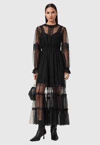 Μαύρο φόρεμα με τούλι που έχει πουά σχέδιο, βολάν στο τελείωμα και διαφανείς μακριές μανίκες. Συνδυάζεται με μαύρη τσάντα χειρός και μποτάκια στον αστράγαλο.