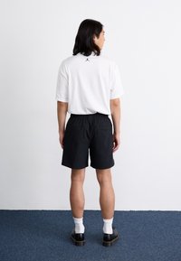 Black shorts with elastic waistband, white t-shirt with a small black logo on the back, paired with white socks and black shoes.