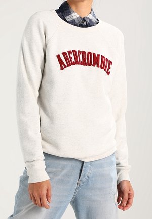 Person wearing white Abercrombie sweatshirt over a blue plaid shirt, paired with light blue ripped jeans.