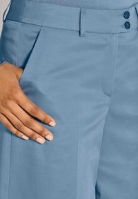 Maßgeschneiderte Hosen aus weichem blauen Stoff mit glatter Textur. Sie verfügen über eine Frontfalte und einen Bund mit zwei Knöpfen, der einen strukturierten Sitz bietet.