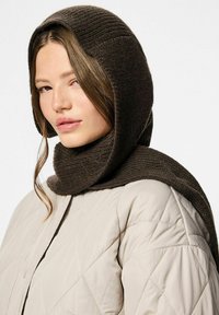 Brun ribbet strikket hætte drapere over en varm beige quilted pufferjakke, der har en høj krave og knaplukning, hvilket skaber et lagdelt look.