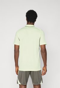 Lichtgroene polo met korte mouwen, een kraag en een rechte zoom, gecombineerd met donkergrijze shorts met lichtgroene accenten.