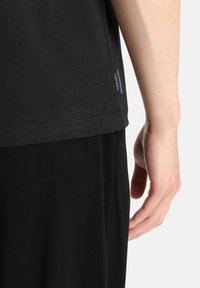 Black short-sleeve t-shirt made from soft fabric with a tag on the side, paired with black pants, showing the back and side of the shirt.