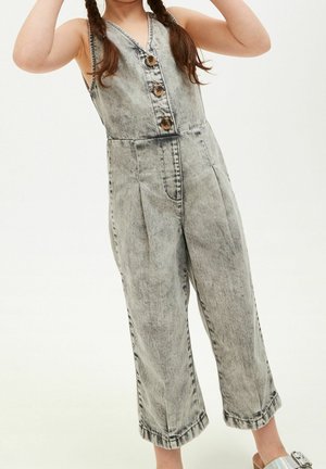 Salopette en denim grise avec un décolleté en V, quatre boutons sur le devant et des jambes larges et cropped. Présente une texture délavée et des poches latérales.