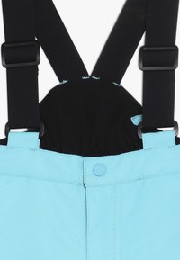 Pantalones de tela azul con tirantes negros ajustables y un cierre de botones a presión en la parte delantera de la cintura.