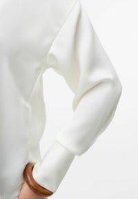 Witte sweatshirt met een zachte, gladde textuur; heeft een loose-fit, puffed mouw en een houten armband om de pols.