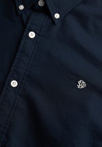 Dark blue button-up shirt with white buttons and a small white embroidered logo on the chest side.