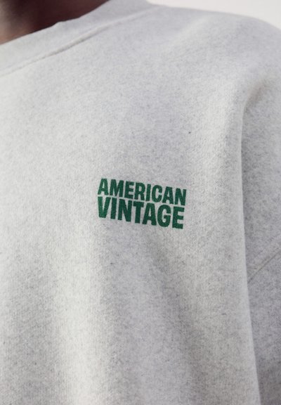 Gros plan d'un sweat-shirt gris clair avec un texte vert ""AMERICAN VINTAGE"" sur la poitrine.