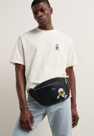 Schwarze Lederbauchtasche mit strukturiertem Finish und einem weißen Cartoon-Charakter-Druck. Hellfarbiges T-Shirt mit kleiner Charakterillustration.