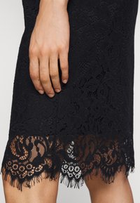 Černá krajková sukně se květinovými vzory, texturovaným povrchem a vlnitým krajkovým lemem s třásněmi na spodním okraji.