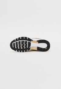 Nike tenisice imaju potplat od crne gume s teksturiranim gripom, bijele akcentne dijelove na srednjem sloju i zlatni uzorak na površini za dodatne detalje.