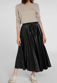 Zwarte geplooide rok van nep leer, met een elastische Tailleband. Gecombineerd met een beige lange mouw top en lichte sneakers.