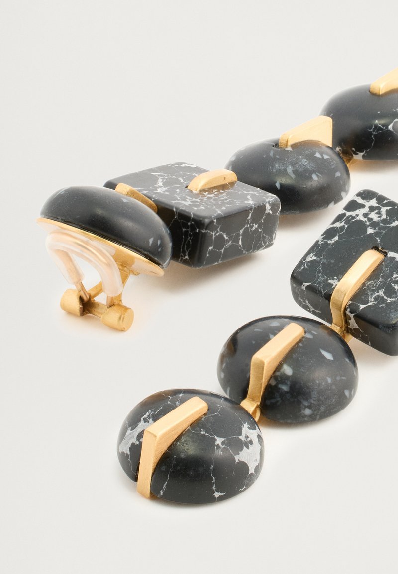 Svart och guldhalsband med rundade och fyrkantiga marmorlika pärlor med vita ådror och guldaccenter, designat med ett lås.