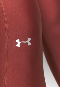 Bordeaux sportleggings met een naadloos ontwerp, gestructureerde stof en een wit logo op de dij. Zichtbare stiksels.