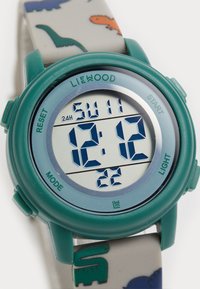Montre numérique avec un boîtier en plastique turquoise et un bracelet gris comportant des motifs de dinosaures colorés. Affiche l'heure en chiffres bleus en gras.