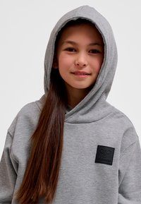 Grå luvtröja i mjukt tyg med stor luva, en logotypmärke på bröstet och en avslappnad passform.