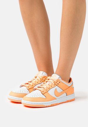 Nike lenkkarit, joissa on sekoitus oranssia ja valkoista synteettistä materiaalia, rei'itetty kärki ja oranssi kumipohja. Nauhat ja yksityiskohdat vastaavat yläosaa.