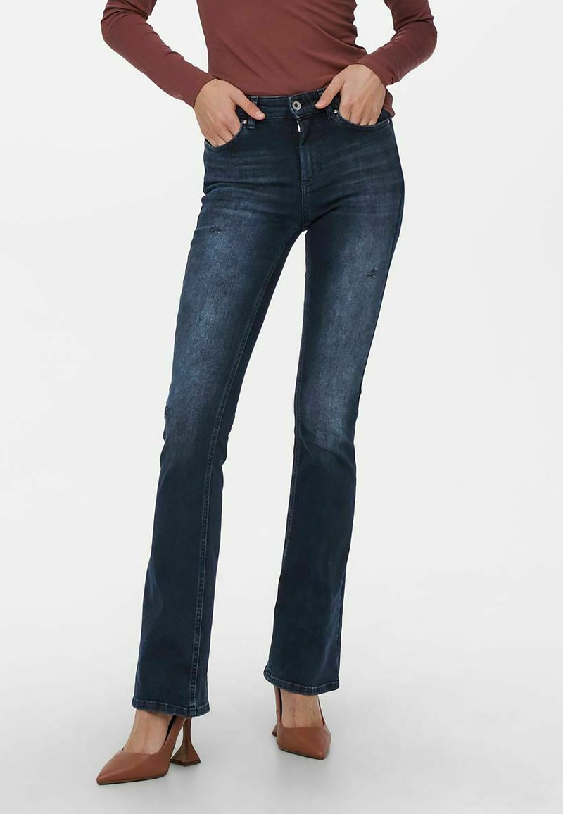 Jean flare bleu foncé avec un léger délavage, taille mi-haute, cinq poches et des détails de couture subtils.