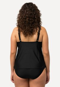 Schwarzes Schwimmoberteil mit verstellbaren Trägern, das eine lockere Passform und eine glatte Textur bietet. Kombiniert mit schwarzen Schwimmhosen, schlichtem und minimalistischem Design.