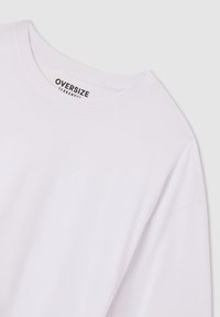 T-shirt bianca oversize con scollatura rotonda. Il tessuto appare liscio e morbido, con un'etichetta stampata nera che riporta la scritta "OVERSIZE TERRANOVA."