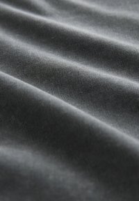 Gros plan sur un tissu gris foncé lisse avec des plis doux et une texture tissée fine visible à la lumière naturelle.