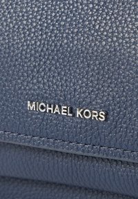 Granatowa torebka z teksturowanej skóry z srebrnym logo „MICHAEL KORS”. Powierzchnia ma ziarnistą fakturę i widoczne przeszycia jako akcenty.