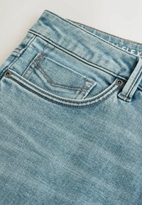 Világoskék farmernadrág klasszikus ötlovas zsebes kialakítással, látható varrással, réz színű fém alkatrészekkel és enyhén megkopott textúrával.